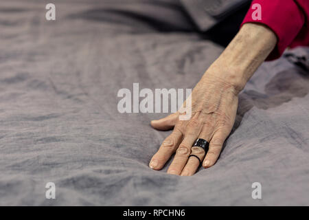 Mug shot du vieillissement madame la main sur lit de draps gris Banque D'Images