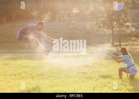 Un jeune couple ludique chassant les uns les autres et jouer avec les pistolets à eau dans un pré ar le coucher du soleil. Banque D'Images