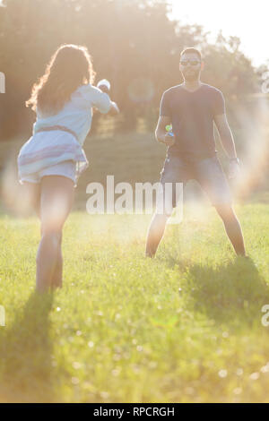 Un jeune couple ludique chassant les uns les autres et jouer avec les pistolets à eau dans un pré ar le coucher du soleil. Banque D'Images
