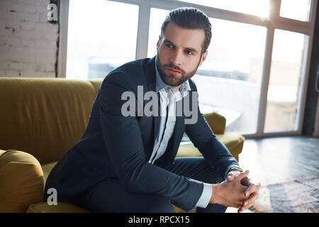 Perdu dans des pensées d'affaires réfléchie...beau jeune homme d'affaires est d'y penser tout en étant assis sur le canapé dans son bureau moderne. Fashion look. Concept d'entreprise. Banque D'Images