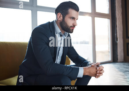 Perdu dans des pensées d'affaires réfléchie...beau jeune homme d'affaires est d'y penser tout en étant assis sur le canapé dans son bureau moderne. Fashion look. Concept d'entreprise. Banque D'Images