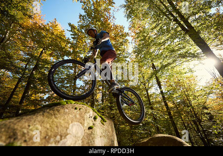 Cycliste professionnel sauter sur trial location sur big boulder. Low angle view of male rider faire tour acrobatique dans la forêt de l'été journée ensoleillée. Concept de sport extrême de vie actif Banque D'Images