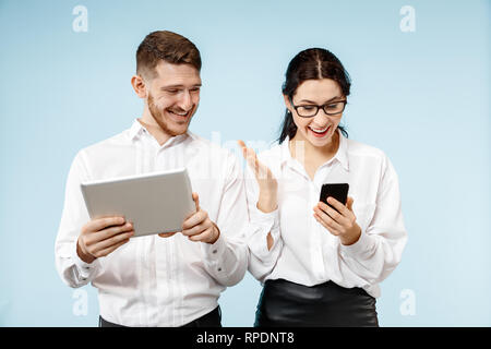Concept de partenariat dans les affaires. Happy smiling Young man and woman standing avec téléphone et tablette contre fond bleu au studio Banque D'Images