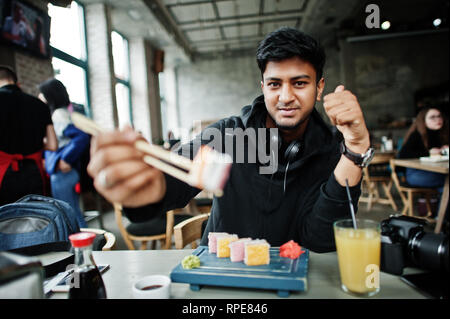 Casual et élégant jeune homme asiatique avec des écouteurs au café de manger des sushis. Banque D'Images