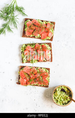 Trois sandwiches avec le pain de seigle, de l'avocat, du saumon fumé sur un fond blanc. Haut de la vue, télévision lay. Banque D'Images