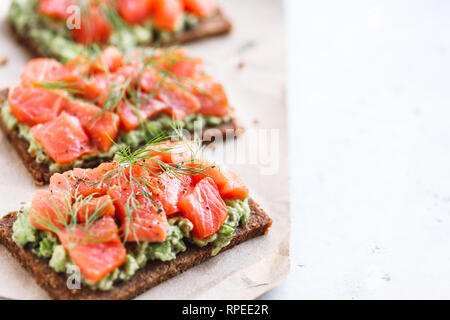 Vue rapprochée de trois sandwiches avec le pain de seigle, d'avocat et saumon fumé, sur une table de cuisine blanche. Copier l'espace. Banque D'Images