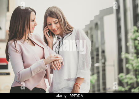 Deux jeunes femmes d'organiser une réunion via un téléphone mobile avec leurs partenaires commerciaux. Contrôle de la femme du temps sur la montre. Banque D'Images