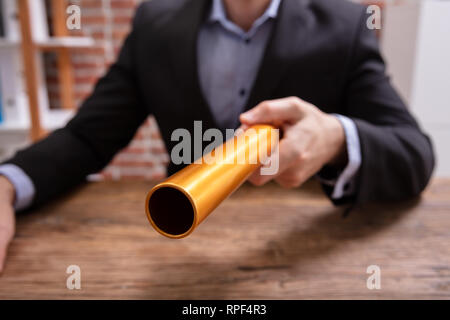 La mi-section of a person's Hand Holding Baton de relais d'Or plus de bureau en bois Banque D'Images