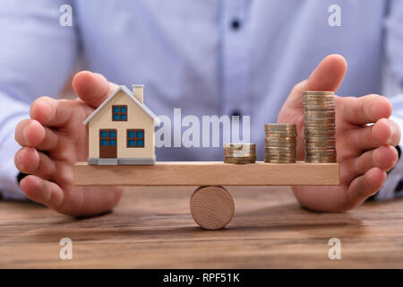 Petite maison modèle et des pièces d'or empilés en équilibre sur la balançoire en bois Banque D'Images