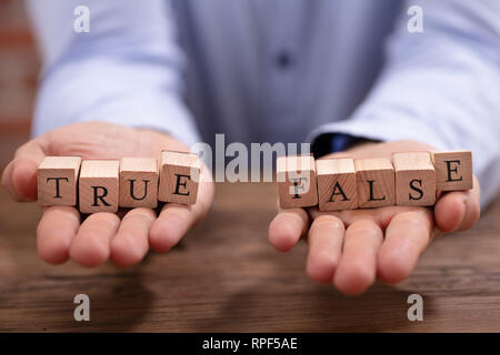 Close-up Man's Hand Holding True et False bloque plus de bureau en bois Banque D'Images