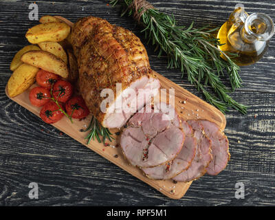 Roulade de porc rôti, en tranches de pomme de terre et de tomate avec le rouleau sur une planche à découper Banque D'Images