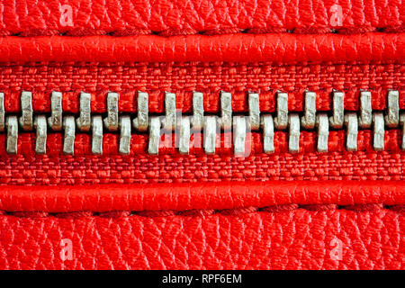 Fermeture éclair en métal sur cuir rouge intense ou un sac à main veste détail close up macro. La fermeture éclair est bien fermé enserrant les deux couches textiles avec t Banque D'Images