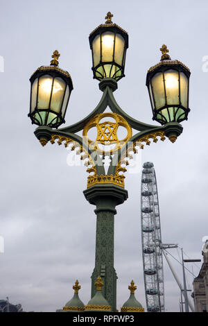 Lampadaire en fonte orné à trois têtes avec lampes à gaz allumées sur Westminster Bridge England London avec l'œil londonien en arrière-plan Banque D'Images
