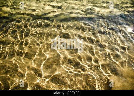 L'eau de mer fait de motifs abstraits et formes ondulant sous un soleil qu'elle lave et ondulations sur une plage de sable Banque D'Images