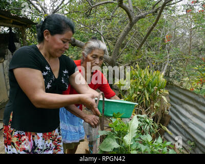 El Salvador COMUS projets près d'Agustin, village d'Calingagua Usulutan. Accueil de Maria del Carmen Benitez (49) chemise noire. Maria et son amie Francisca Rodriguez Granadina (chemise rouge) arrosage jardin potager. Banque D'Images