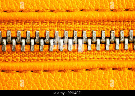 Fermeture éclair en métal sur veste en cuir orange intense ou bourse détail close up macro. La fermeture éclair est bien fermé enserrant les deux couches textiles wit Banque D'Images