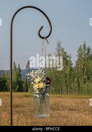 Pot Mason de jaune, rouge foncé, et blanc gypsophile fleurs en suspension dans une prairie de montagne pour marquer l'allée à un mariage. Banque D'Images