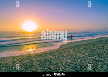 Silhouette surfeur marche sur la plage de l'océan au coucher du soleil Banque D'Images