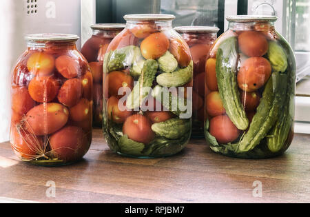 Accueil préservation : grands pots en verre rouge mûre avec tomates et concombres au vinaigre, couvercle métallique scellée. Banque D'Images