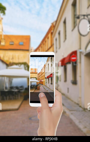 Un homme fait une photo de la rue européenne vide avec café dans la vieille ville de Vilnius sur un téléphone mobile Banque D'Images