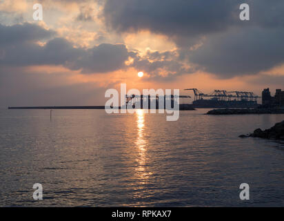 Soleil reflétant dans l'eau du port au coucher du soleil grandes grues en arrière-plan Banque D'Images