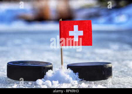 Un drapeau suisse sur les cure-dents entre deux rondelles de hockey. La Suisse va jouer sur une coupe du monde en groupe B. 2019 Championnat du Monde de Hockey sur glace en B Banque D'Images