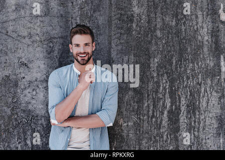 Heureux jeune homme habillé en décontracté élégant bleu chemise et T-shirt gris, avoir une attitude décisive, smiling and looking at camera, isolé sur fond gris. Concept de réussite Banque D'Images