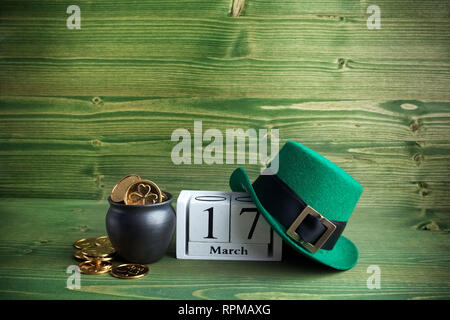 Bloc blanc calendrier pour St Patrick's Day, le 17 mars, avec chapeau de Leprechaun et pot d'or, sur fond de bois vert. Banque D'Images