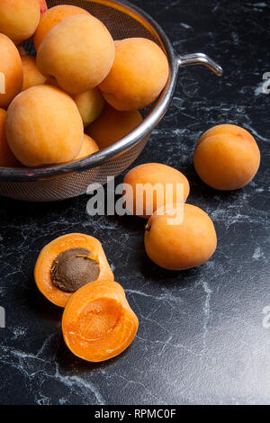 Organique mûres les abricots dans une passoire en acier. Composition dans un style rustique - jaune bio abricots juteux dans son ensemble et passoire en acier et des moitiés d'abricots o Banque D'Images