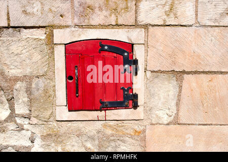 Une petite porte rouge voûté avec metal higes sur un mur de pierre Banque D'Images