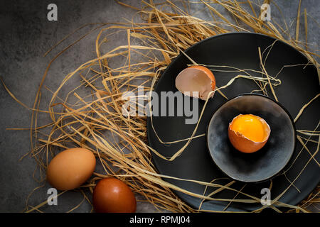 Oeuf cassé avec des oeufs entiers sur une plaque sombre sur fond sombre Banque D'Images