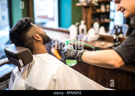 Jeune homme assis dans la chaise de coiffure cheveux peignage et la pulvérisation du petit enfant avec les mains de coiffure Banque D'Images