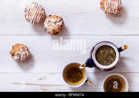 Tasses à thé, théière et muffins sur la table en bois blanc, Set théière et thé infusé avec des feuilles séchées de gâteaux sur la table, vert noir boisson chaude à base de plantes en por Banque D'Images