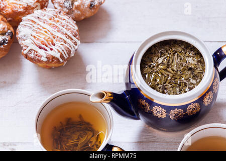 Tasses à thé, théière et muffins sur la table en bois blanc, Set théière et thé infusé avec des gâteaux sur la table, vert noir boisson chaude à base de plantes en pot en porcelaine, e Banque D'Images