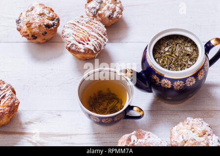 Tasses à thé, théière et muffins sur la table en bois blanc, Set théière et thé infusé avec des gâteaux sur la table, vert noir boisson chaude à base de plantes en pot en porcelaine, e Banque D'Images