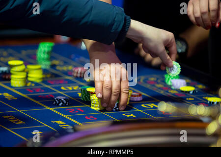 Table de roulette avec des mains de poser des jetons dans un casino. La roue de roulette à l'avant-plan. Jouer jeu. Les gens méconnaissables. Banque D'Images