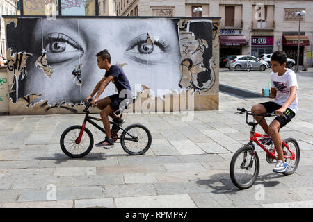 Livourne - garçons sur les bicyclettes à proximité d'une affiche déchirée d'un visage de femme sur la Piazza de Republica. Banque D'Images