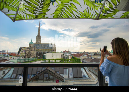 Une jeune femme prend une photo de Stephansdom avec son téléphone portable depuis le bar sur le toit de l'hôtel Lamée à Vienne, Autriche Banque D'Images