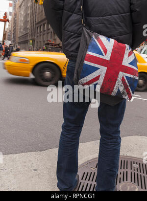 Homme debout au coin de rue avec British Union drapeau sur son ordinateur et d'un taxi en passant par la ville de New York, Manhattan, USA Banque D'Images