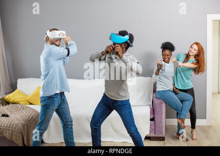 Groupe d'étudiants de sexe masculin féminin multiraciale amd jouer jeu virtuel en utilisant des lunettes de vr, de s'amuser ensemble ay accueil - Réalité Virtuelle salut et portable di Banque D'Images