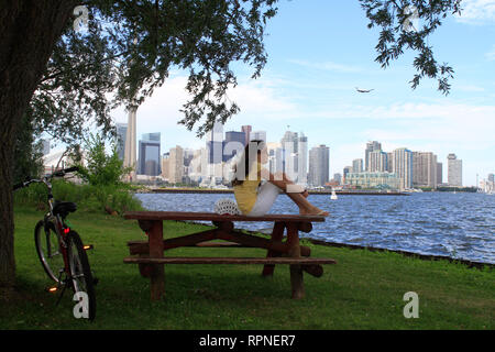 Dix ans, fille, et se repose sur une table de pique-nique du parc sur l'île Centre contre un paysage urbain de Toronto (Ontario) au Canada. Banque D'Images