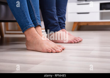 La section basse des pieds du couple sur le plancher dans la salle de séjour Banque D'Images