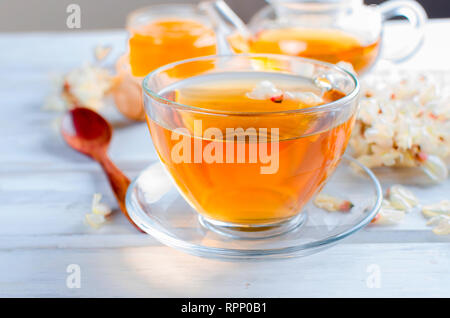 La guérison d'une tisane avec du miel de fleur d'acacia brassé dans une théière et de branche d'acacia sur la vieille table en bois blanc rustique. Banque D'Images