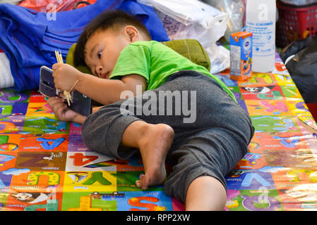 Enfant jouant à des jeux sur un téléphone, Chiang Mai Banque D'Images