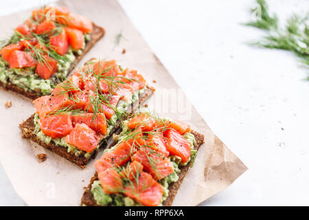 Vue rapprochée de trois sandwiches avec le pain de seigle, d'avocat et saumon fumé, sur une table de cuisine blanche. Copier l'espace. Banque D'Images