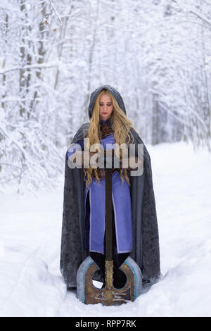 Warrior girl aux cheveux blonds et aux gros ax en forêt d'hiver Banque D'Images