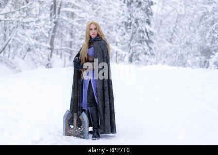 Warrior girl aux cheveux blonds et aux gros ax en forêt d'hiver Banque D'Images