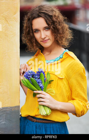 Heureux mode jeune femme avec bouquet de fleurs walking in city street modèle féminin élégant portant chemise jaune et bleu jupe Banque D'Images