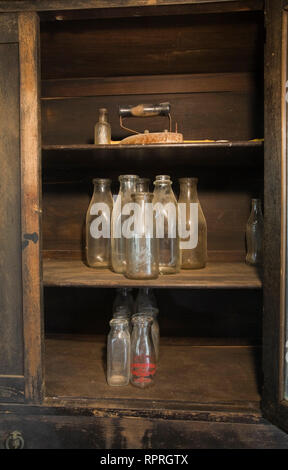 Close-up de quelques vieilles bouteilles de lait à l'intérieur d'un meuble ancien dans la cuisine d'une vieille maison de style cottage Canadiana 1826 Banque D'Images