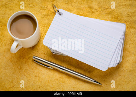 Pile de fiches vierges avec une tasse de café et un stylo contre le papier texturé jaune Banque D'Images